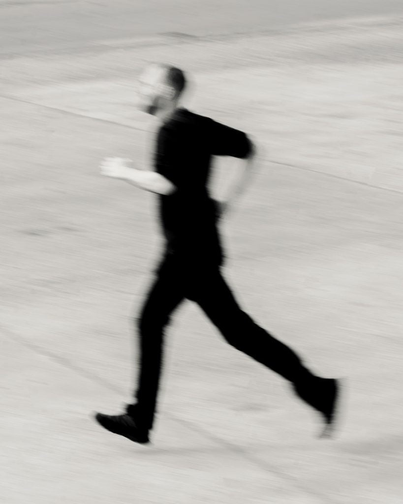 A blurry black-and-white photo of Thor Pedersen running across a concrete surface.