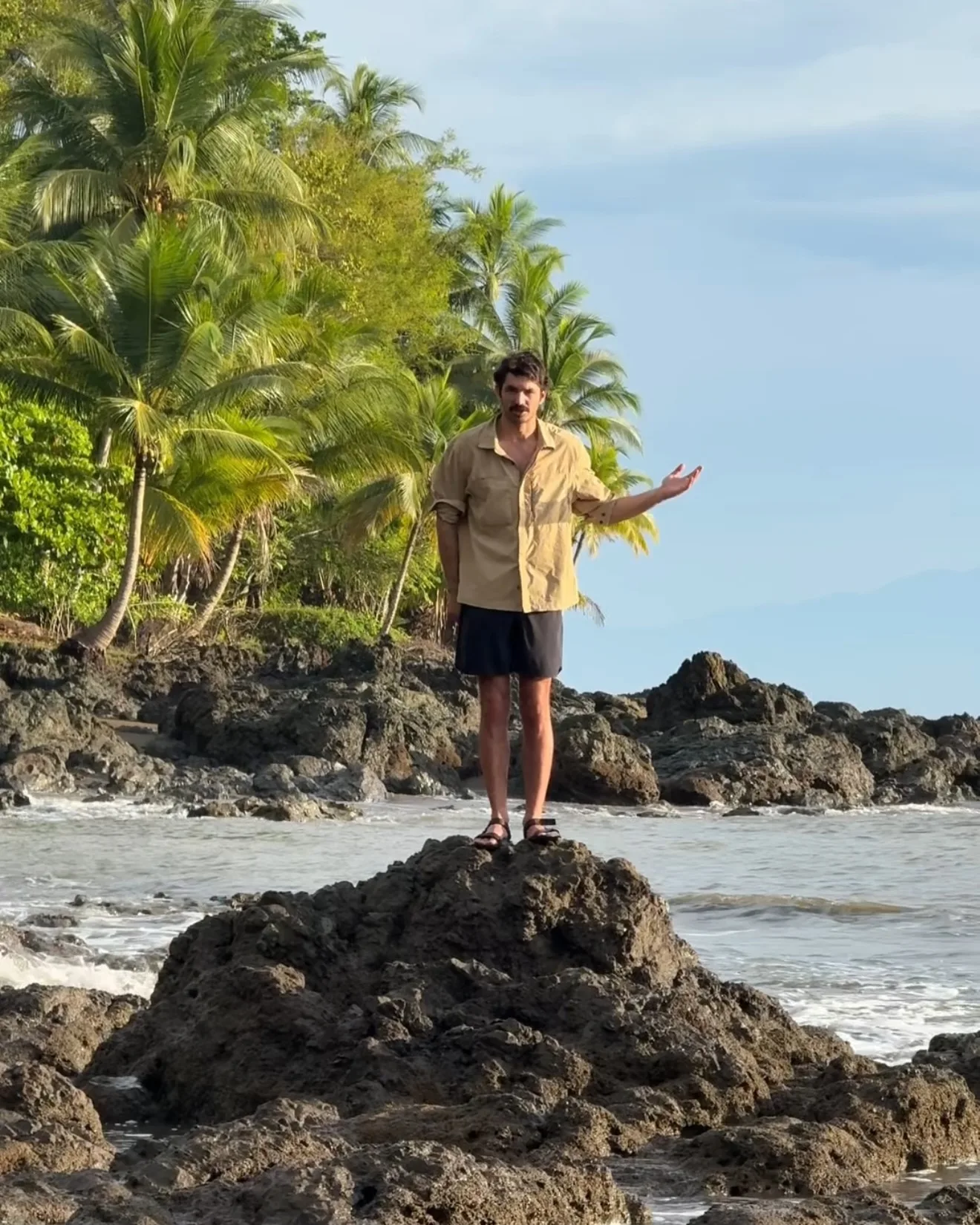 Ben Kielesinski photographed standing on a rock on the shore of Costa Rica, gesturing to the landscape around him.